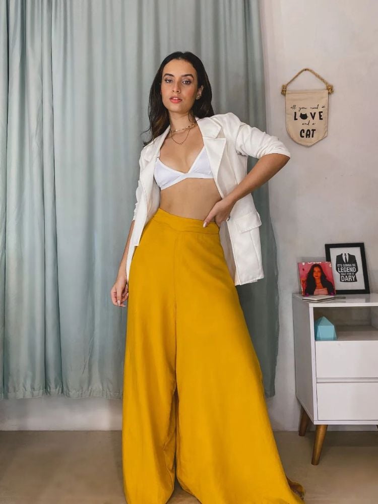 Mulher de pele clara usando sutiã branco, blazer branco e calça larga amarela