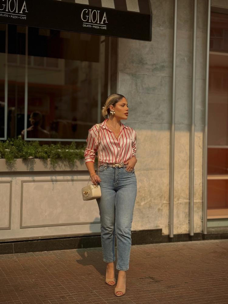 Mulher de pele clara usando camisa de seda branca e vermelha com calça jeans reta clara e sandália de salto