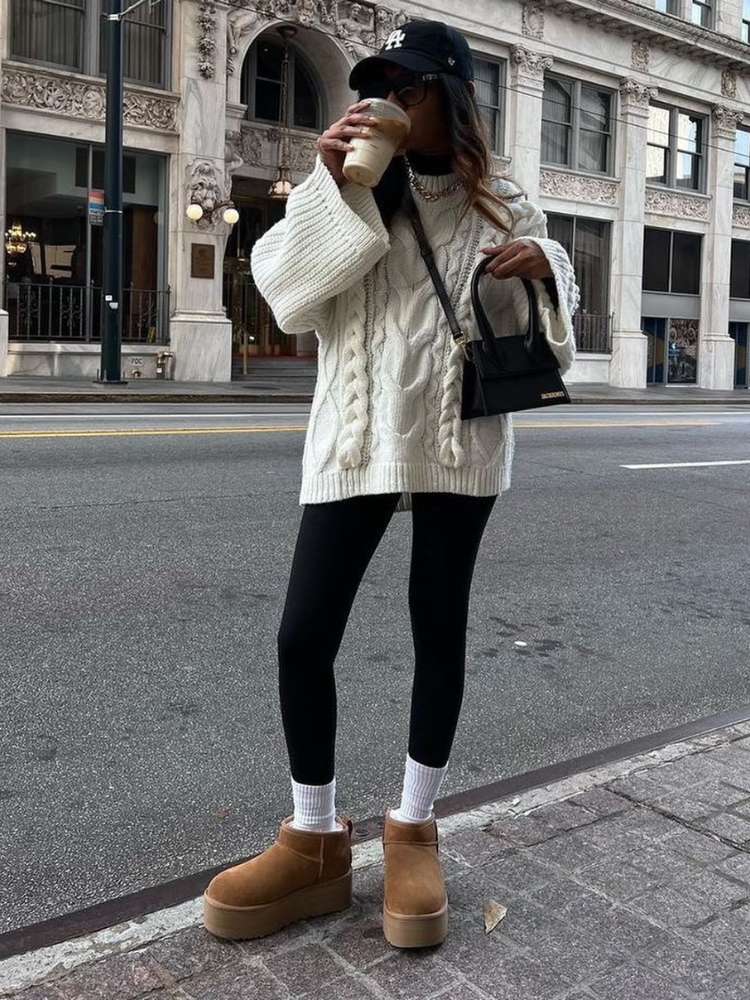 Mulher de pele clara usando suéter oversized branco, legging preta, meia cano médio e ugg boots 