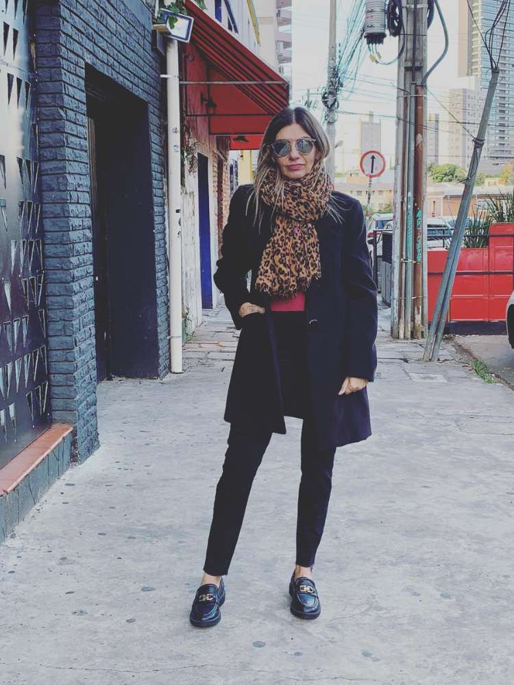 Mulher de pele clara usando blazer preto, cachecol de animal print, calça preta e mocassim preto 