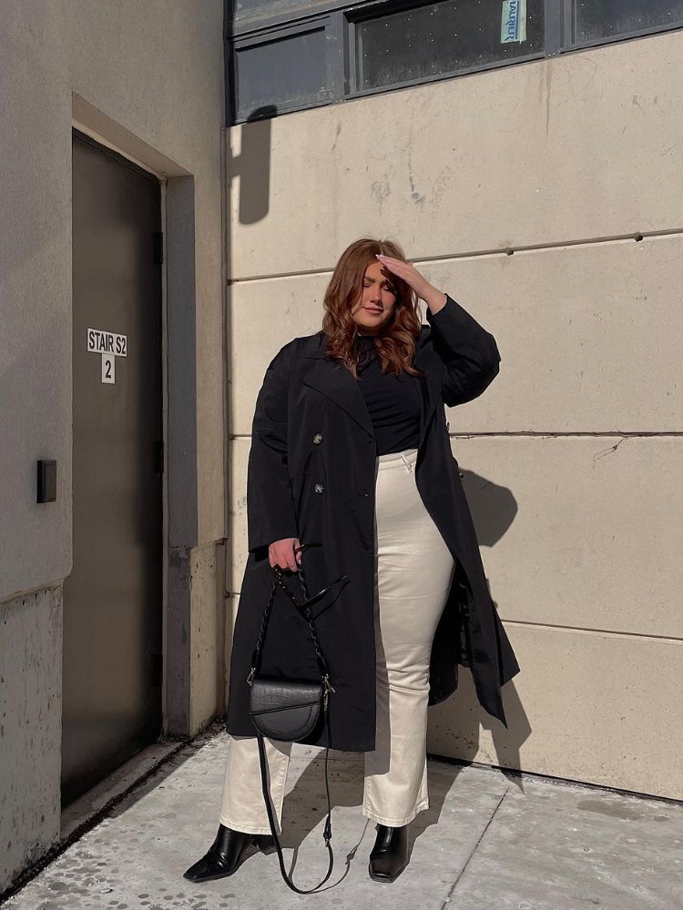 Mulher de pele clara usando blusa preta de gola, calça social bege e sobretudo preto