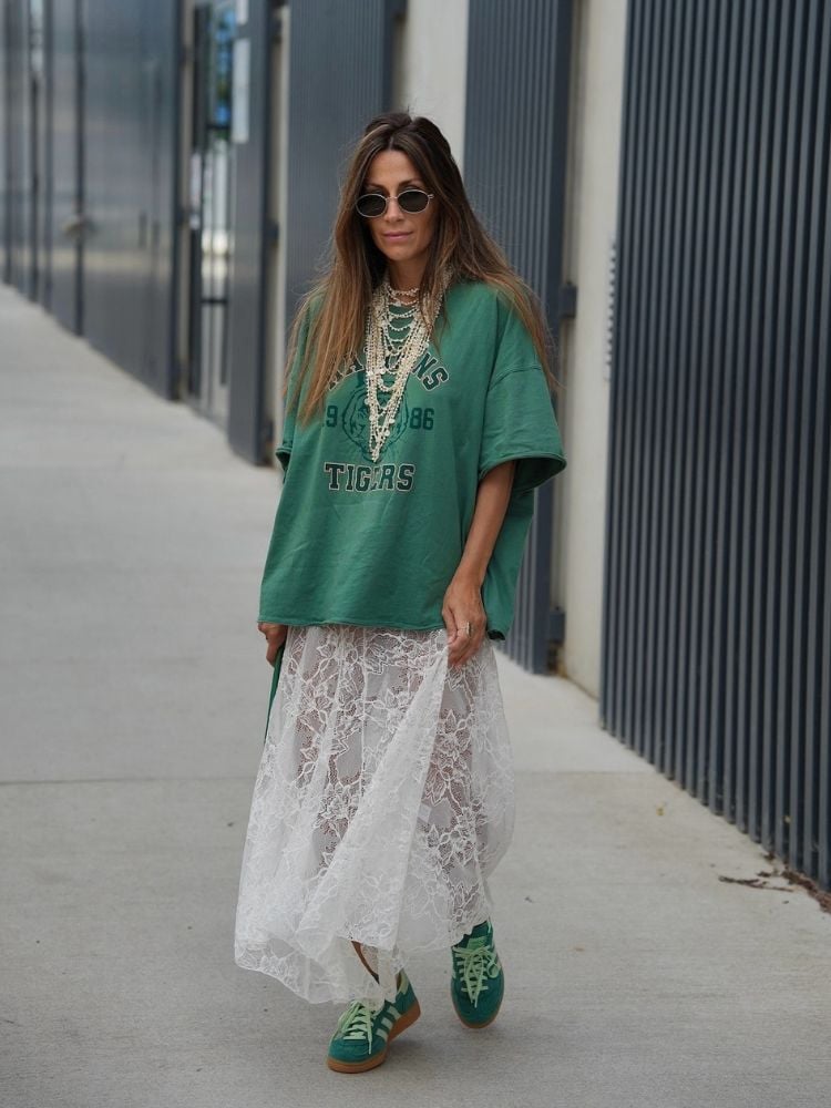 Mulher de pele clara usando blusa verde, acessórios, saia midi de renda branca e tênis verde