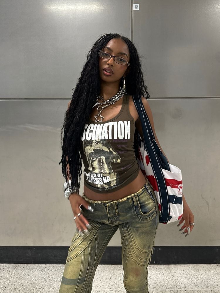 Mulher de pele negra usando regata marrom, calça jeans baixa, acessórios e bolsa 