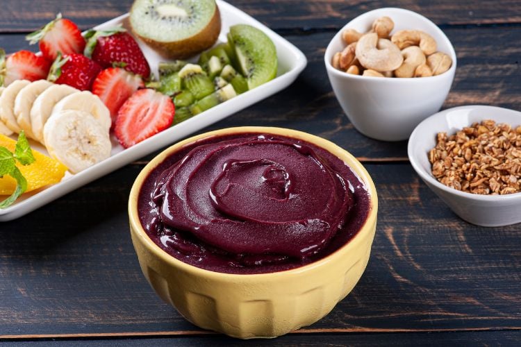 Tigela amarela com açaí e potes brancos com frutas e castanhas 