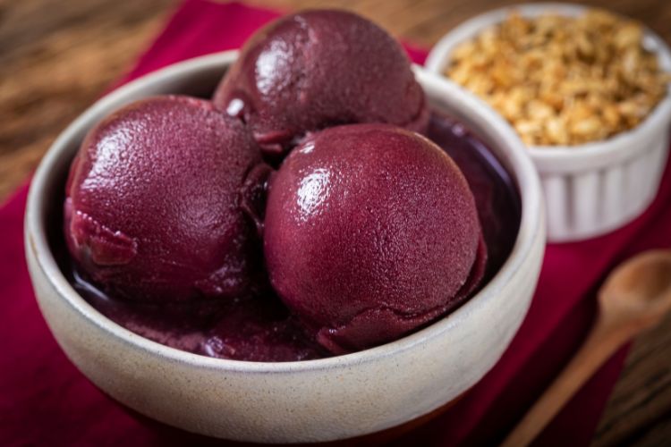 Tigela branca de açaí com pote com nozes ao fundo