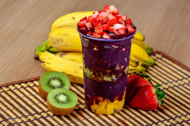 Copo de açaí com banana, kiwi e morango e mesmas frutas ao fundo