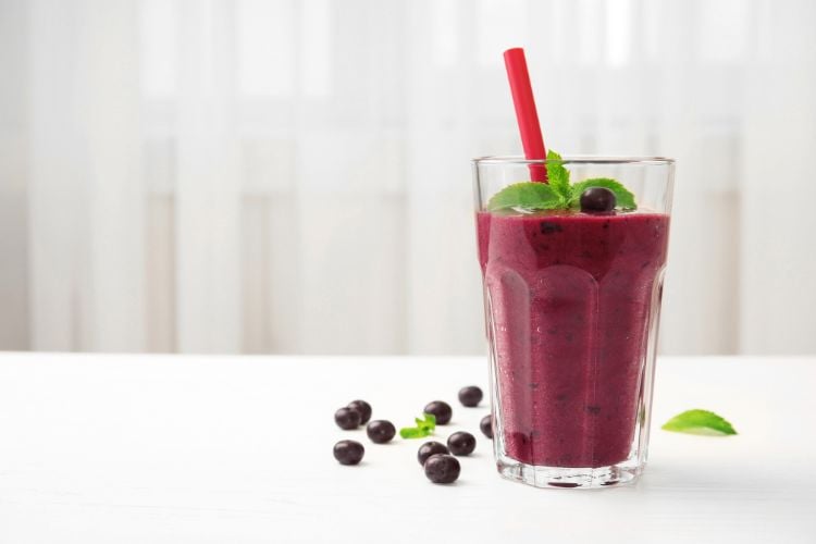 Copo de vidro com smoothie de açaí e canudo vermelho sobre mesa branca