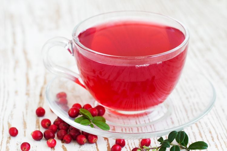 Chá vermelho de cranberry, com frutas ao redor, em xícara e pires transparente
