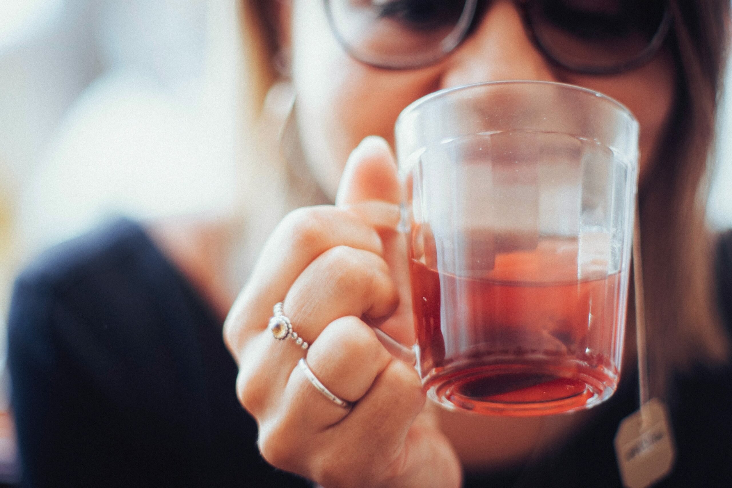 Mulher de pele clara usando óculos de grau e blusa azul, bebendo chá em xícara que imita copo americano