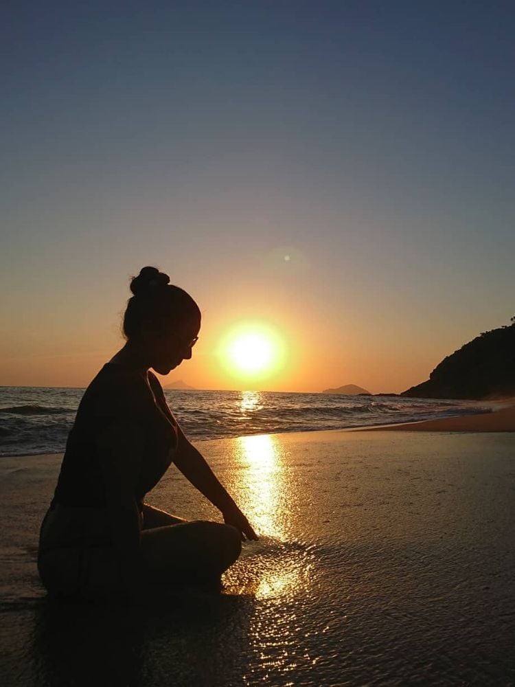 Sombra de mulher sentada à beira do mar em pôr do sol na praia 