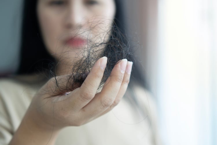 Mulher de pele clara desfocada ao fundo, segurando muitos fios escuros de cabelo 