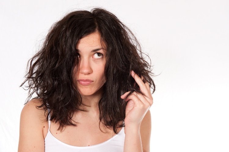 Mulher de pele clara usando regata branca e segurando cabelo com expressão preocupada 