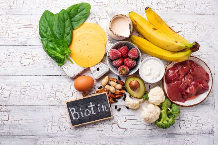 Foto de mesa com couve, queijo, frutas vermelhas, abacate, nozes, banana, ovo e outros alimentos com vitamina B7