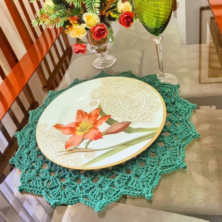 A primeira imagem mostra uma mesa de jantar decorada com um sousplat de crochê verde, sobre o qual há um prato com desenho de flor laranja. Ao lado, um copo verde e um arranjo de flores.