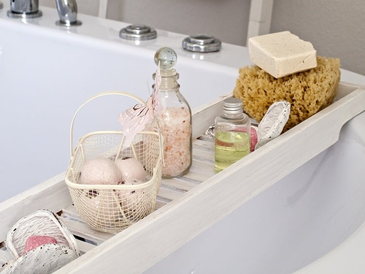 banheira branca com produtos para banho ao lado, como sabonetes, esponja e sais de banho