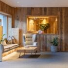 Foto de espaço zen com parede de madeira, sofá na janela com almofadas, chão de carpete bege, vaso alto com planta, mesa de centro de madeira e poltrona bege