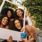 Foto de mulheres de pele negra sorrindo, segurando quadrado que imita polaroid