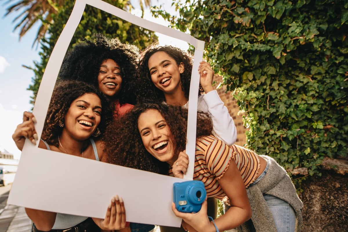 Foto de mulheres de pele negra sorrindo, segurando quadrado que imita polaroid