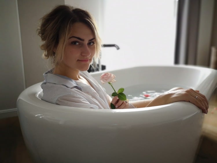 mulher dentro de uma banheiro, com roupão e segurando uma rosa clara nas maõs