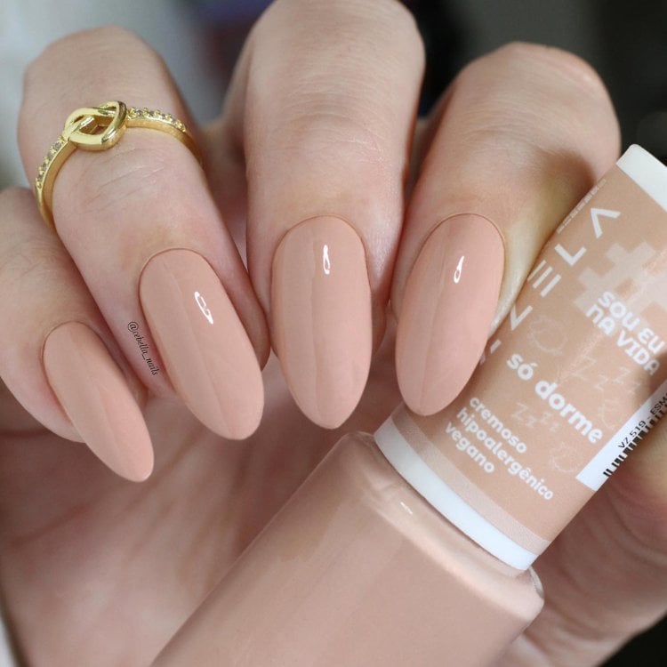 Mulher de pele clara usando unha nude almond, segurando o esmalte