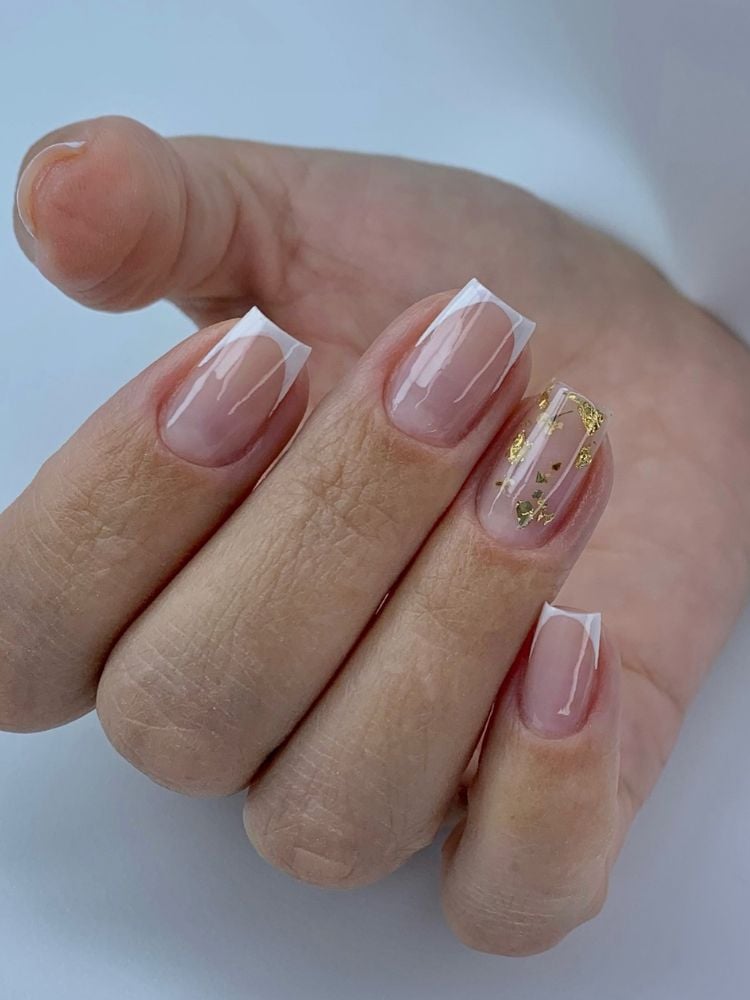 Mulher de pele clara usando unhas quadradas com francesinha e folhas de ouro no anelar