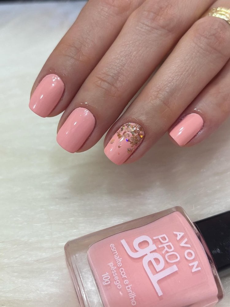 Mulher de pele clara usando unhas quadradas curtas pêssego, com glitter no anelar