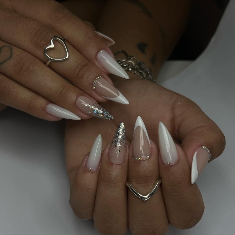 Mulher de pele morena usando unhas stiletto com brilho, francesinha e milky nails