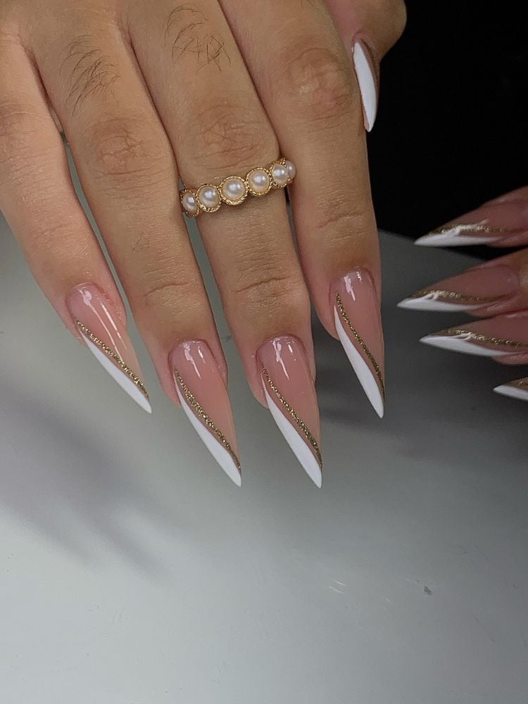 Mulher de pele clara usando unha stiletto com base nude, detalhes finos em branco e dourado