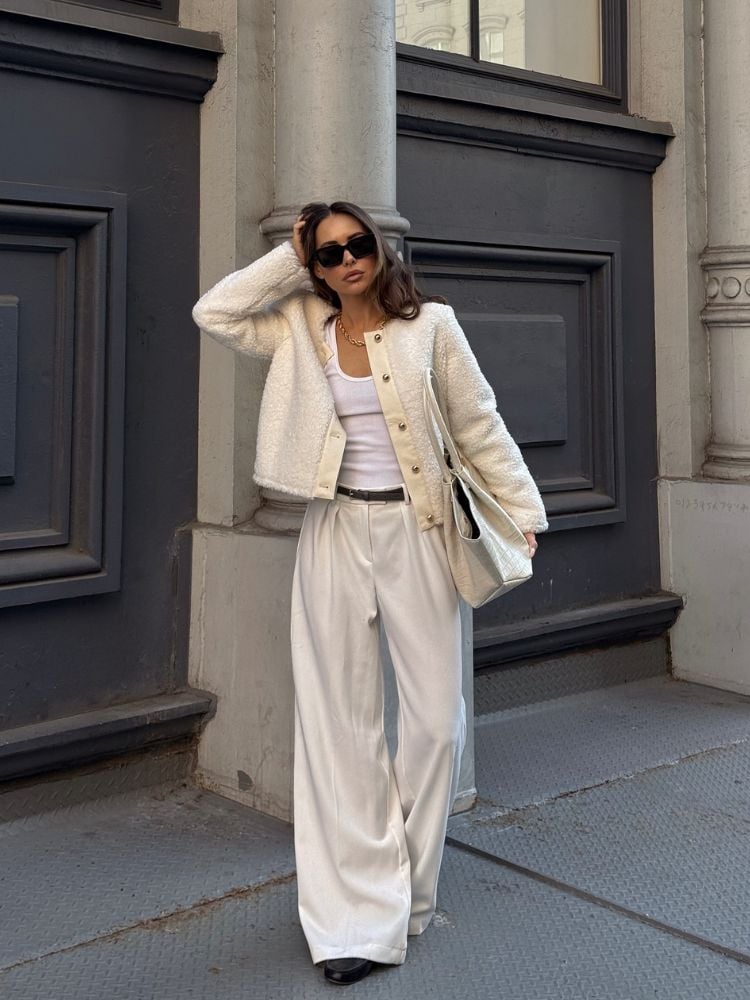 Foto de mulher de pele clara usando casaco de lã bege, blusa branca e pantalona bege