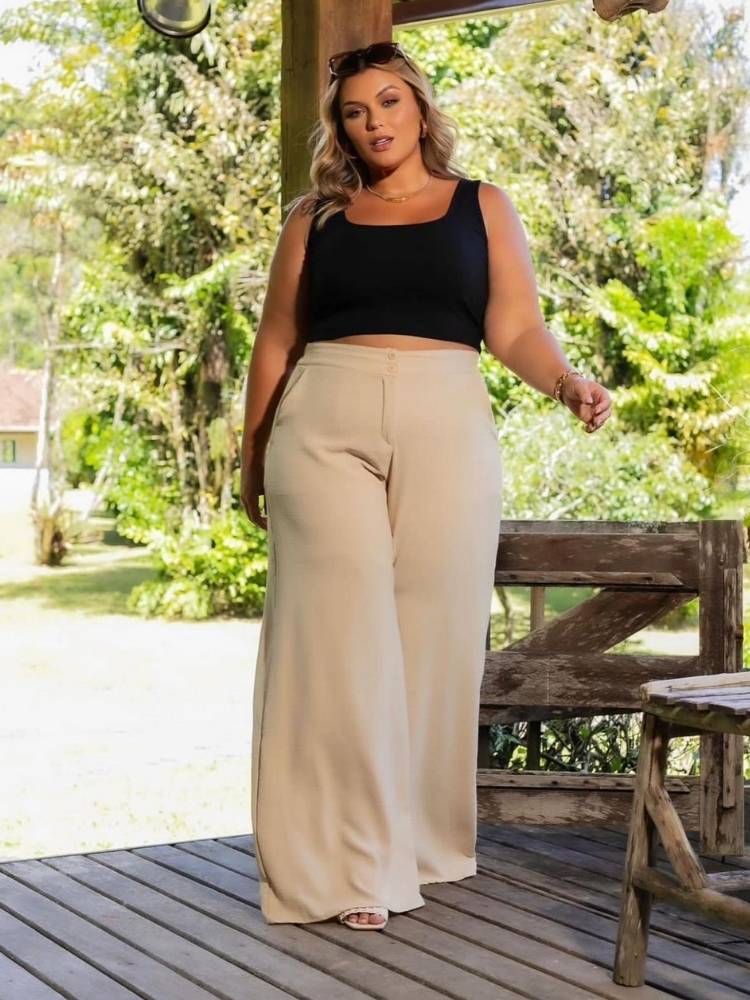 Mulher de pele clara em ambiente com plantas, usando cropped preto de alça e pantalona bege