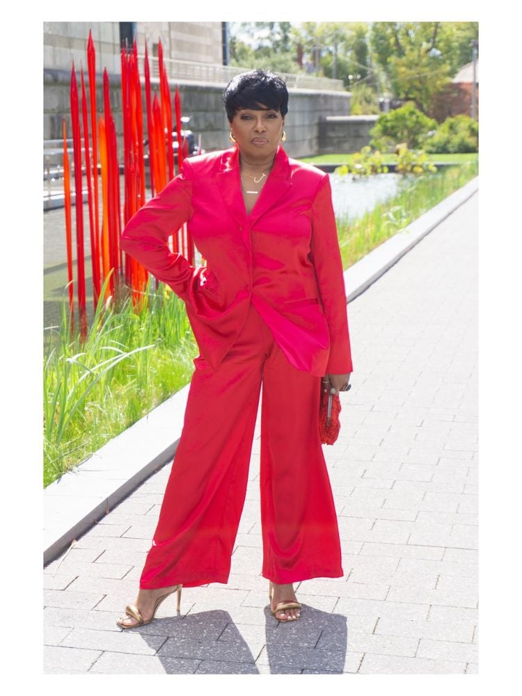 Mulher de pele negra usando blazer rosa fechado, pantalona rosa um pouco mais curta e salto alto