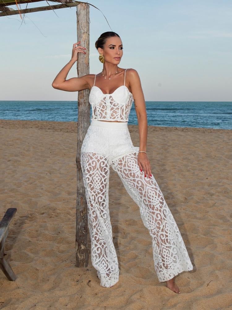 Mulher de pele clara na praia usando cropped e calça pantalona brancos de renda