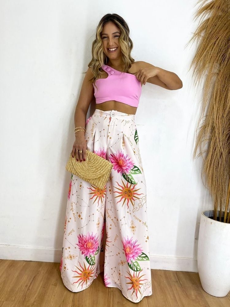 Mulher de pele clara usando cropped rosa e pantalona estampada de sol e flores rosas