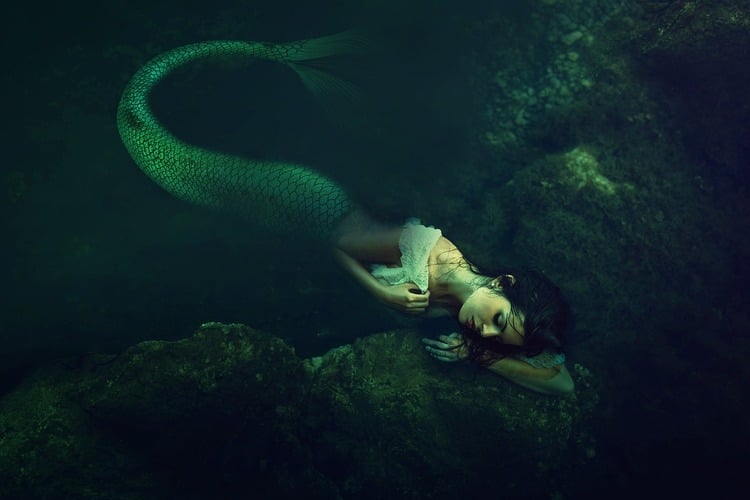 Sereia no fundo do mar olhando de forma sombra para baixo com os braços ao redor do corpo