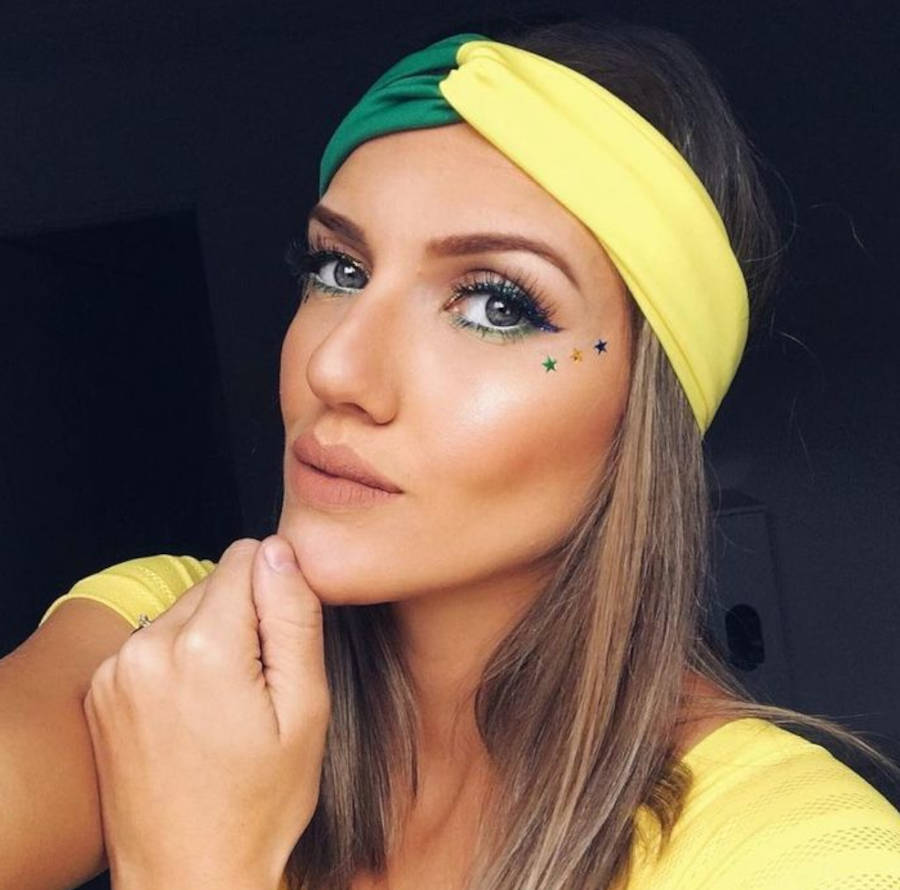 Foto de mulher loira maquiada para a copa do mundo com faixa verde e amarela na testa