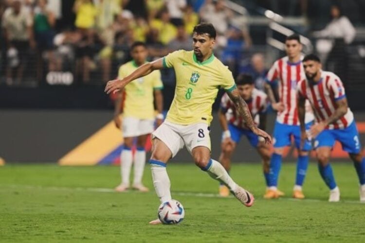 Paquetá em campo com a camisa da Seleção Brasileira, chutando a bola contra o Paraguai, cujos jogadores estão desfocados ao fundo