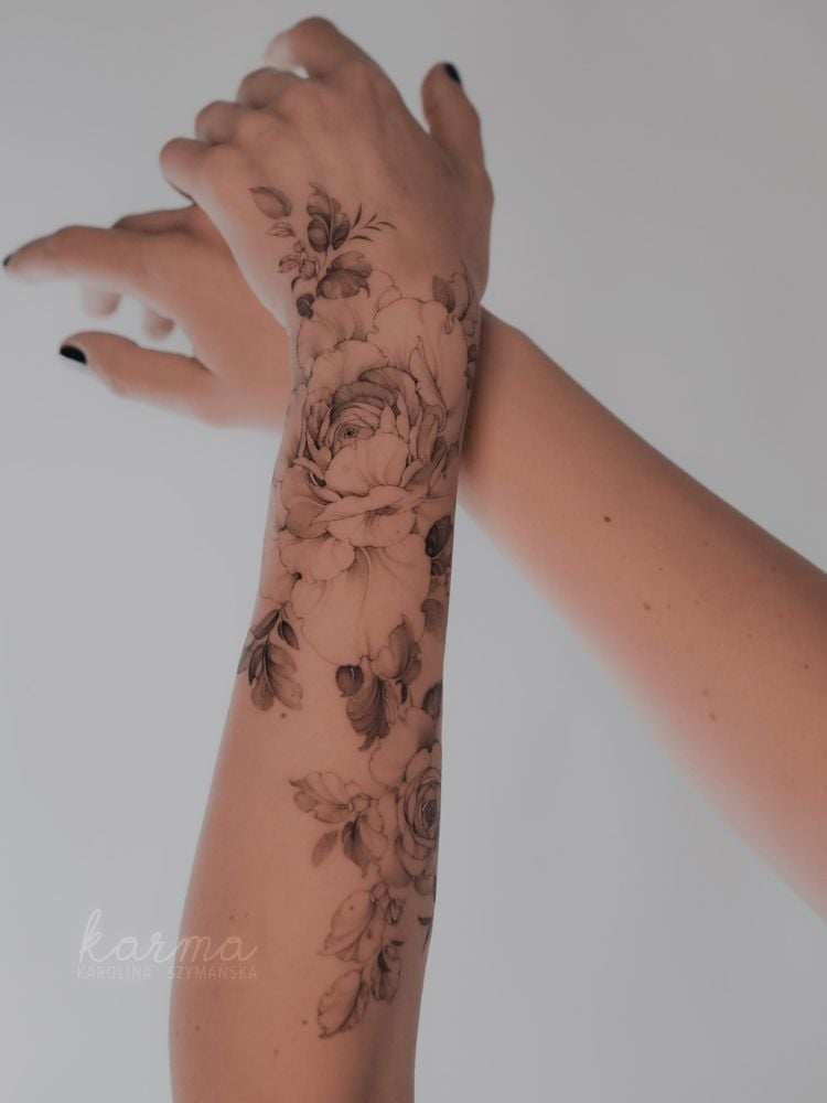 Dois braços de pele clara sendo um deles com tatuagem de flores no pulso que se estende pelo braço 