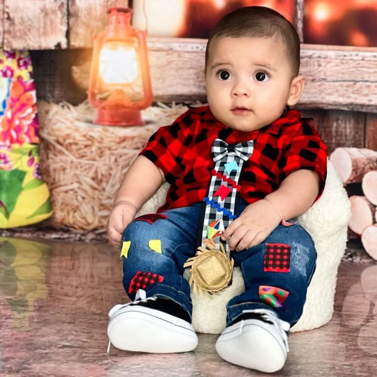 Bebê menino usando blusa xadrez vermelha e preta com gravata xadrez e calça jeans com remendos coloridos