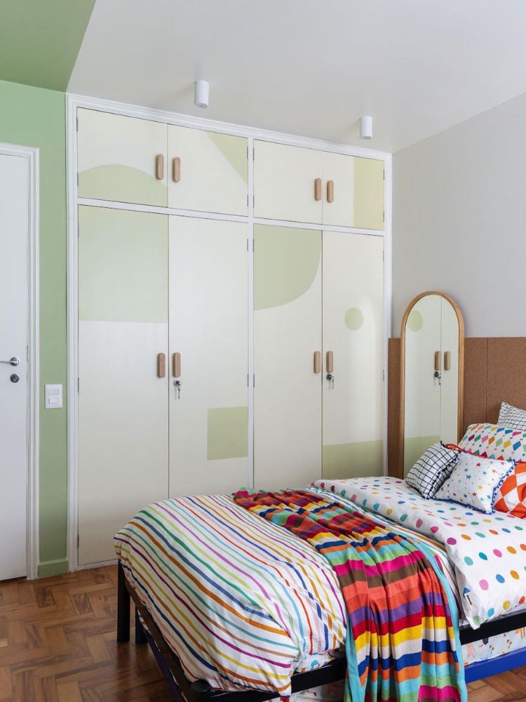 Quarto com paredes brancas, marrom e verde, além de armário branco e verde com roupa de cama colorida