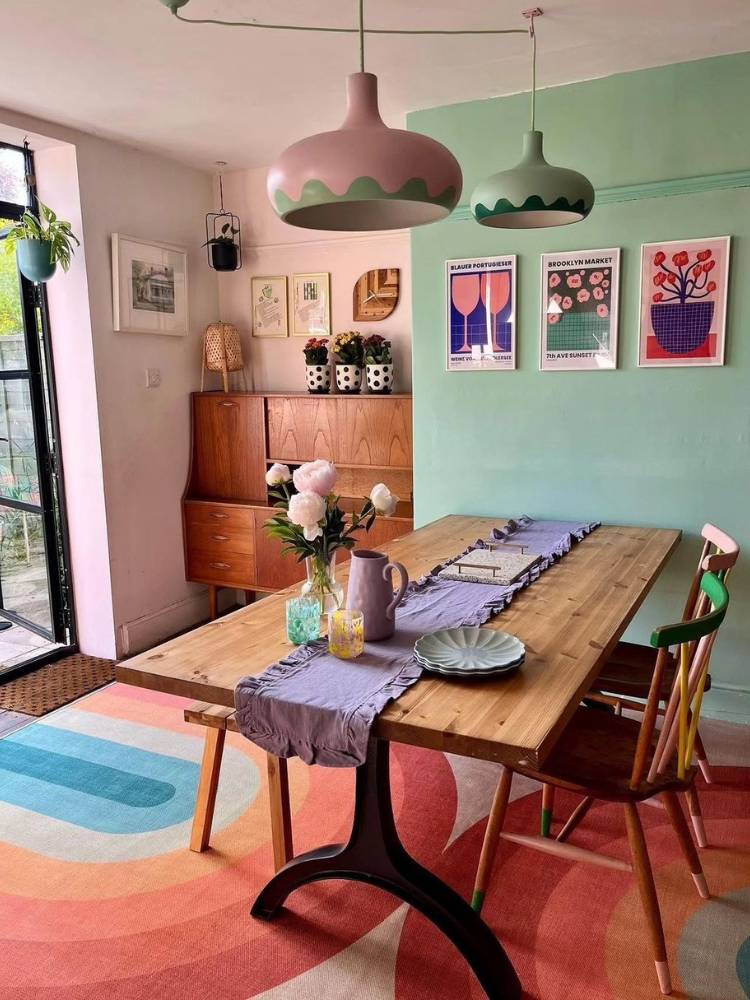 Sala de jantar com parede verde, quadros coloridos, mesa de madeira, caminho de mesa roxo e tapete de arco iris