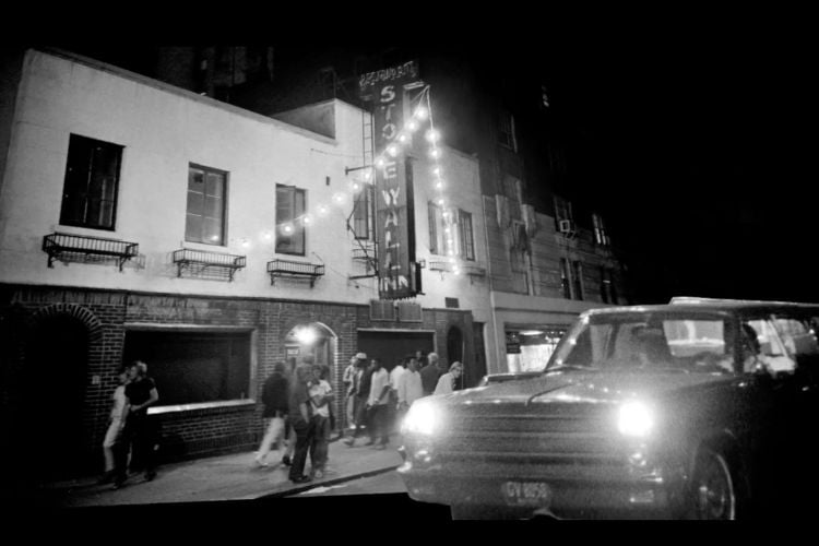 Foto em preto e branco de bar Stonewall antigamente, com luzes, pessoas e carros