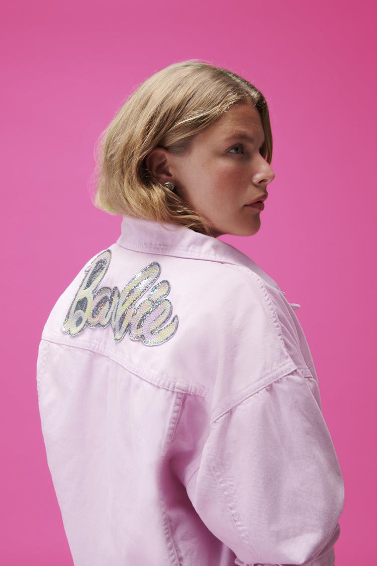 mulher de costas mostrando jaqueta jeans rosa claro da barbie