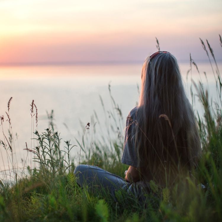 mulher sentada em grama de costas olhando para lago