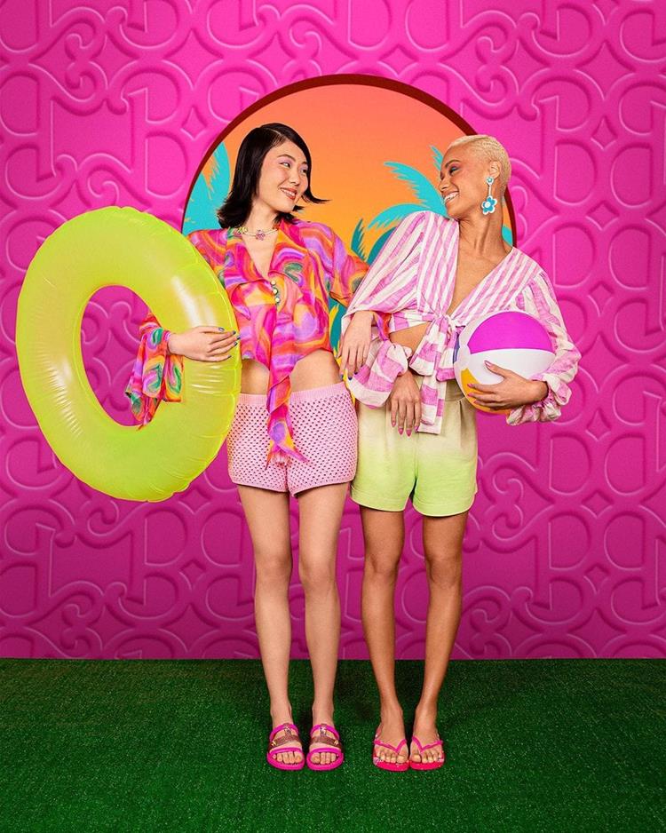 duas mulheres com shorts e camisa de praia com chinelo ipanema da barbie rosa