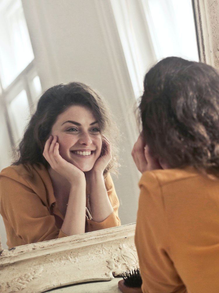 Mulher sorrindo para o espelho para post sobre legendas para fotos sorrindo