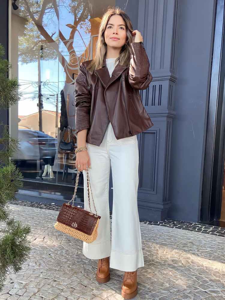 Looks com couro: mulher usando camiseta branca, calça branca, jaqueta marromd e couro, bolsa de palha e couro, bota de couro bege