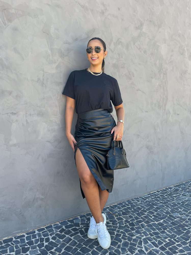 Looks com couro: mulher usando camiseta pretao, saia midi de couro com fenda, bolsa preta e tênis branco