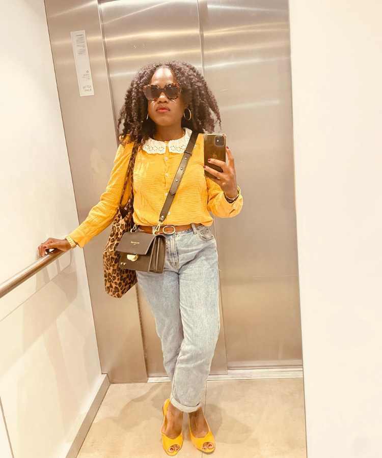 Imagem com fundo de elevador. Foto de mulher no espelho usando blusa amarela + calça jeans + sapatilha amarela + bolsas marrom e com estampá de onça