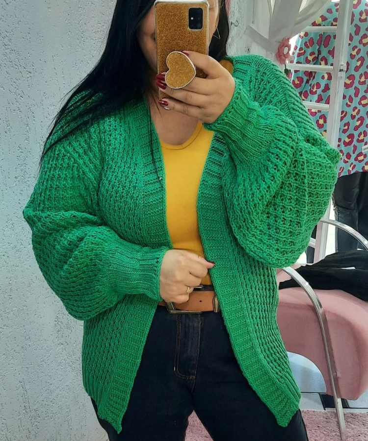 Imagem com fundo de parede e cadeira. Foto no espelho mulher usando regata amarela, casaco de lã verde, calça jenas e cinto