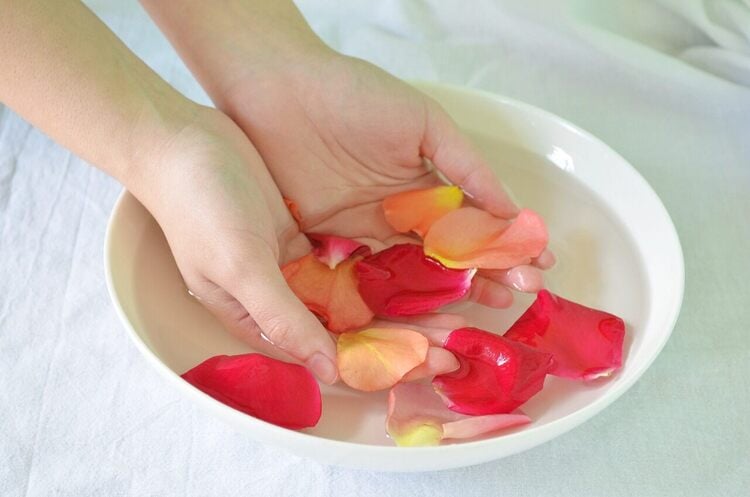 mãos femininas em um recipiente com água e pétalas de rosas